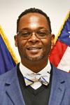 man facing forward wearing bow tie with flags behind him