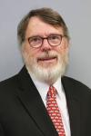 Man wearing glasses with white beard, suit and red tie