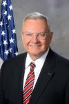 man in black suit with red tie and american flag in the background