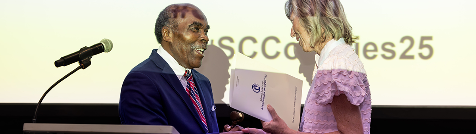 Outgoing SCAC President Bill Robinson passes the gavel to 2025-26 SCAC President Mary Anderson.