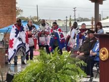 Military veterans stand on a stage, draped in red-white-and-blue quilts made as part of the Quilts for Valor project. 