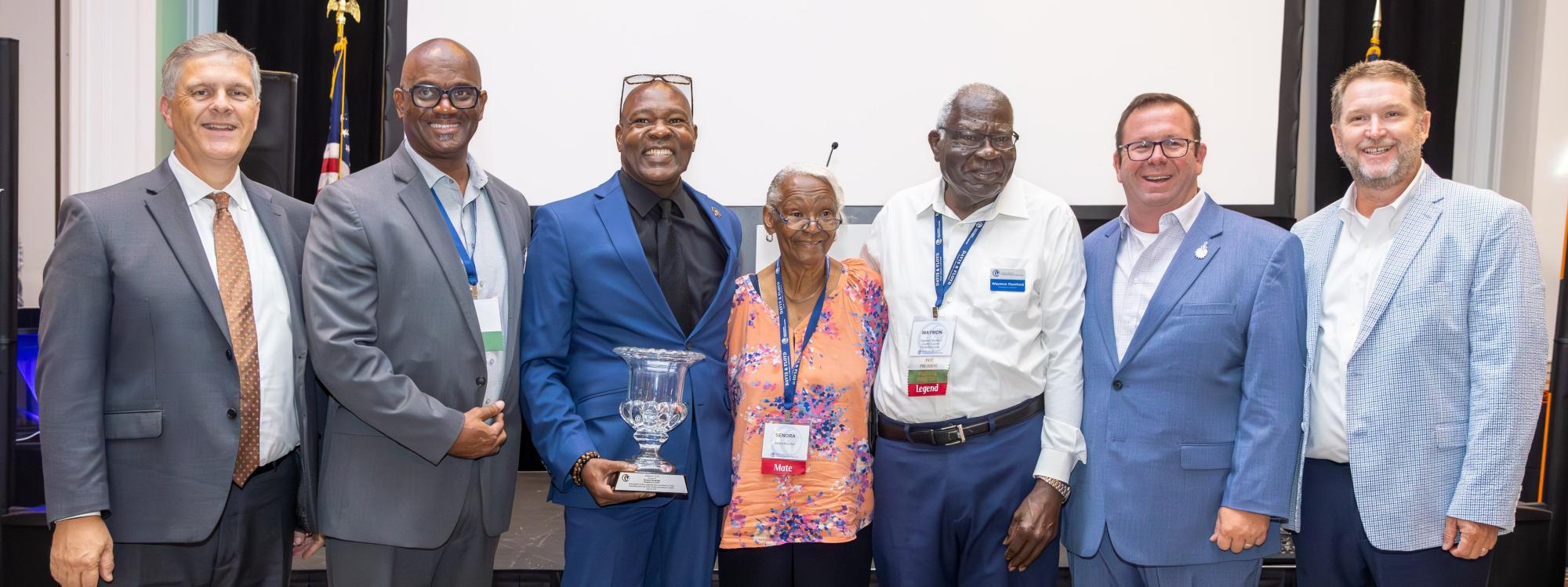 A group of Florence County officials stand in a ballroom with President's Cup honoree Rev. Waymon Mumford in the center of the group. 