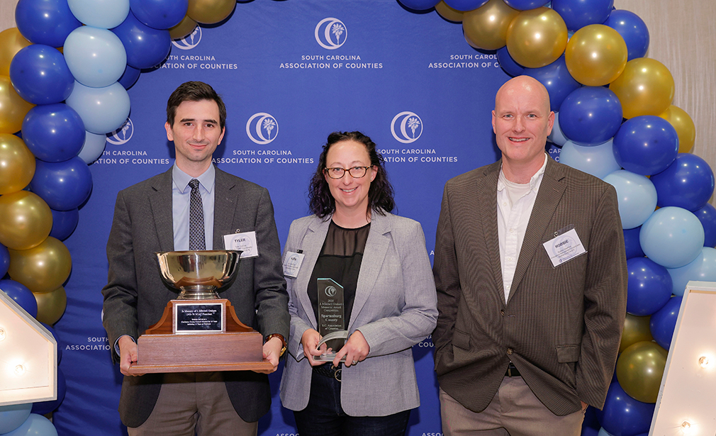 two men and one woman hold SCAC awards in front of a blue background