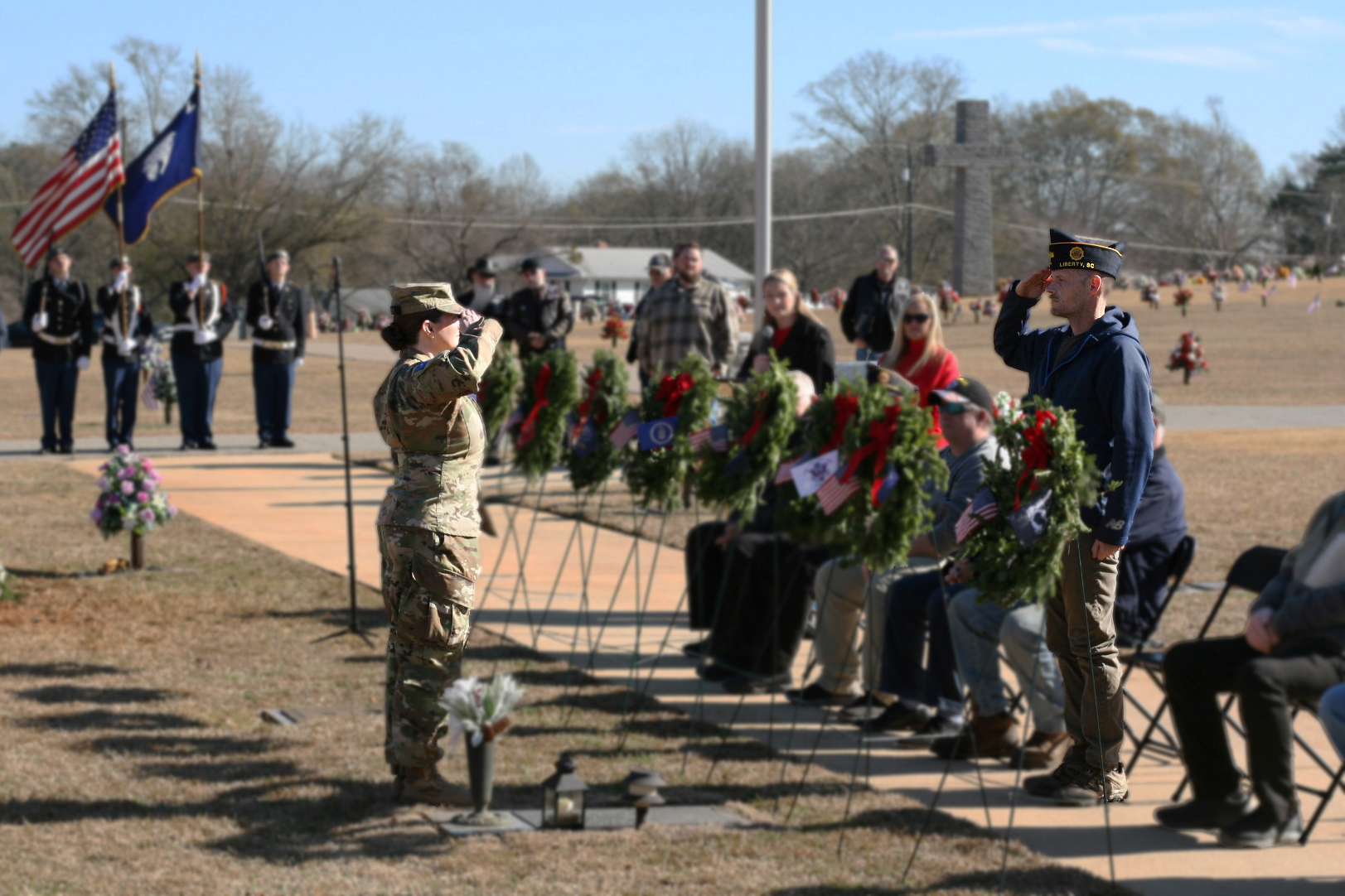 A female soldier salutes another service member at a wreath-laying ceremony.