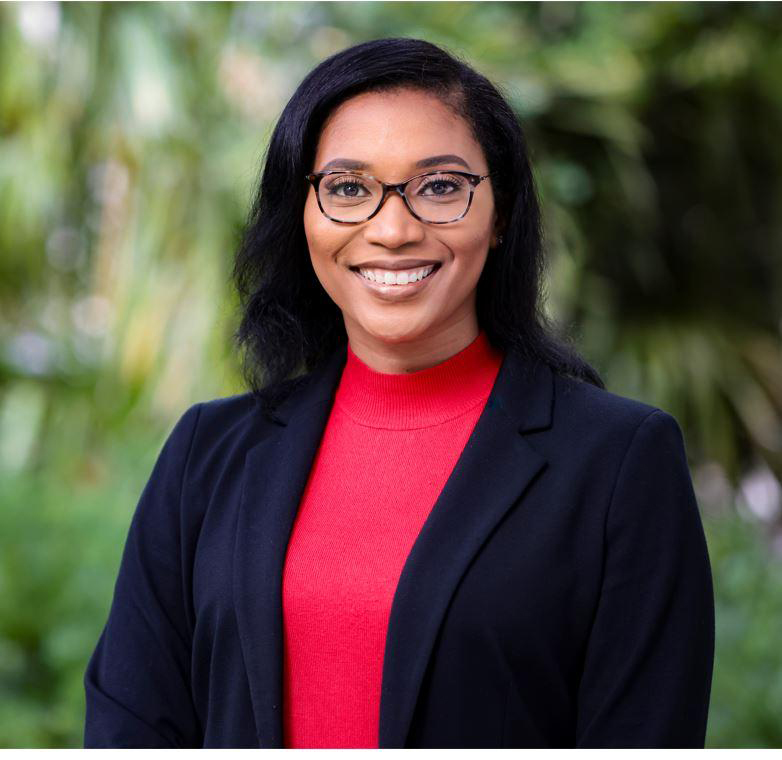 Black woman wearing glasses, a red shirt and a black blazer in front of a green background